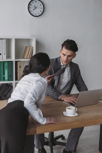 Sensual secretaria tocando lazo de guapo hombre de negocios mientras lo seduce en la oficina - foto de stock