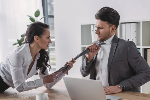 Secretaria sexy tocando corbata de hombre de negocios mientras lo seduce en la oficina - foto de stock