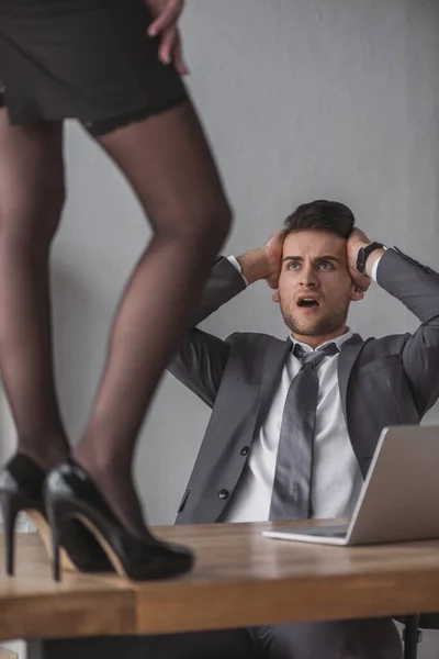 Abgeschnittene Ansicht einer Sekretärin, die in hochhackigen Schuhen auf dem Schreibtisch steht, in der Nähe eines schockierten Geschäftsmannes — Stockfoto