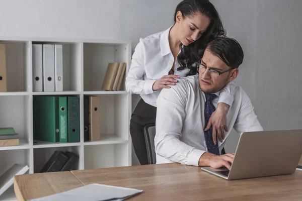 Sexy empresária abraçando confuso colega sentado no local de trabalho — Fotografia de Stock