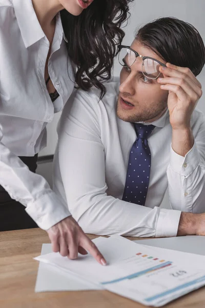 Sorprendido mujer de negocios mirando el pecho de sexy colega sentado cerca de él en el escritorio — Stock Photo