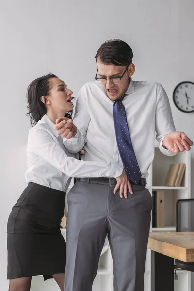 Passionate businesswoman touching trousers of shocked colleague while seductive him in office — Stock Photo