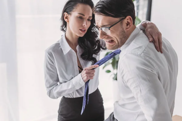 Сексуальна секретарка тримає краватку і обіймає наляканого хлопця, спокушаючи його в офісі — стокове фото
