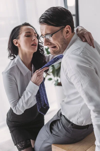 Sexy secretary holding tie and hugging scared boyfriend while seducing him in office — Stock Photo
