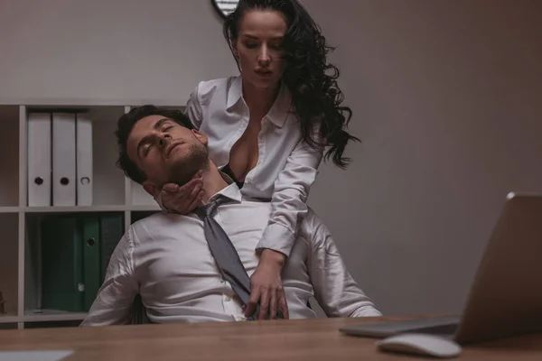 Verführerische Sekretärin in aufgeknöpfter Bluse umarmt gutaussehenden Geschäftsmann sitzend mit geschlossenen Augen — Stockfoto