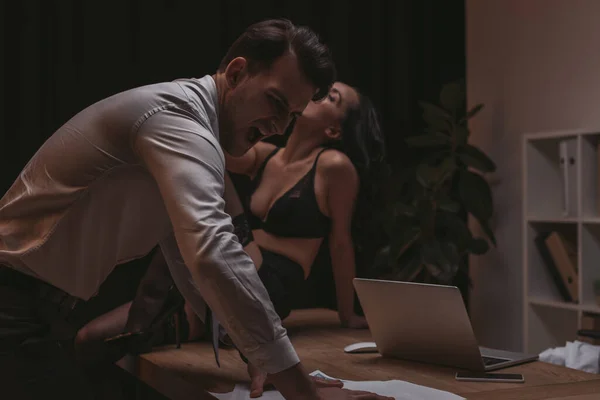 Angry businessman screaming while standing ner papers while sexy secretary sitting on desk in lingerie — Stock Photo