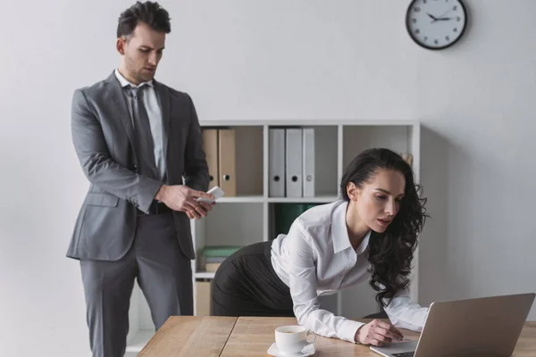 Handsome businessman taking picture of buttocks of secretary standing at workplace — Stock Photo