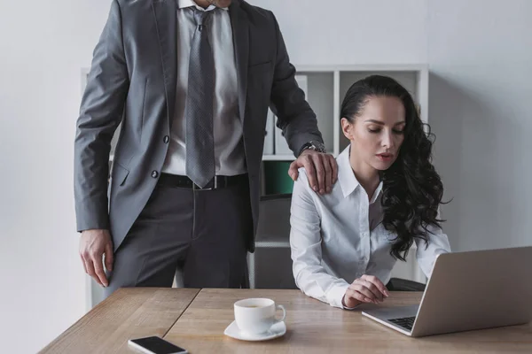 Abgeschnittene Ansicht eines Geschäftsmannes, der Schulter einer Sekretärin berührt, die am Laptop arbeitet — Stockfoto