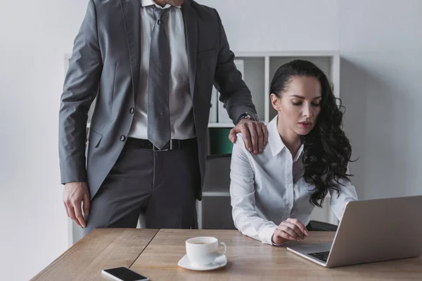 Cropped view of businessman touching shoulder of secretary working on laptop — Stock Photo