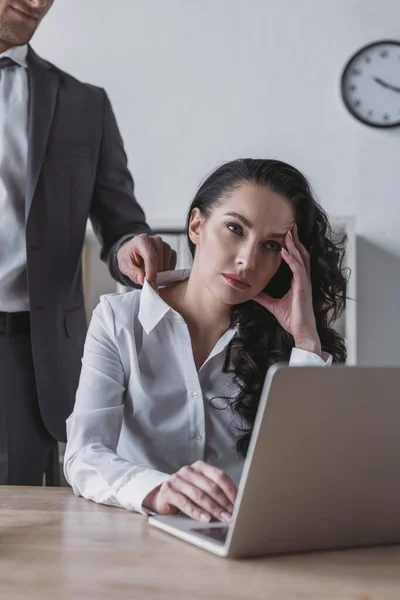 Abgeschnittene Ansicht eines Geschäftsmannes, der die Bluse einer gelangweilten Sekretärin berührt, die am Arbeitsplatz sitzt — Stockfoto