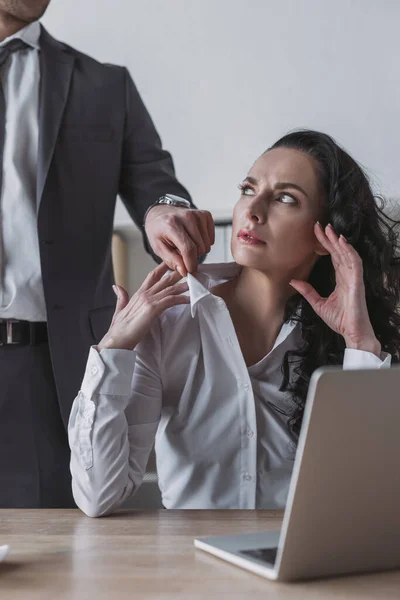 Vue recadrée de l'homme d'affaires touchant chemisier de secrétaire en colère assis sur le lieu de travail — Photo de stock