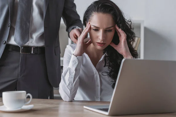 Abgeschnittene Ansicht eines Geschäftsmannes, der die Schulter einer müden Sekretärin berührt, die am Laptop sitzt — Stockfoto