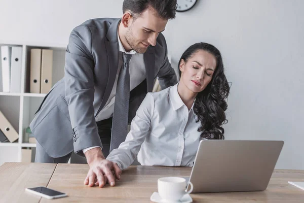 Bel homme d'affaires touchant la main du secrétaire mécontent assis sur le lieu de travail — Photo de stock