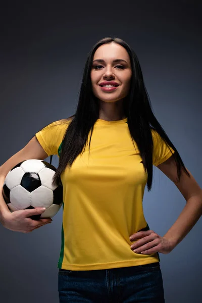 Hermosa chica sonriente sosteniendo pelota de fútbol en gris - foto de stock