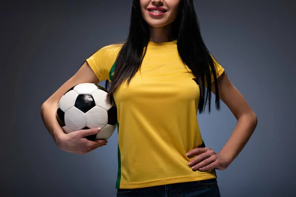 Vista cortada de menina bonita segurando bola de futebol no cinza — Fotografia de Stock