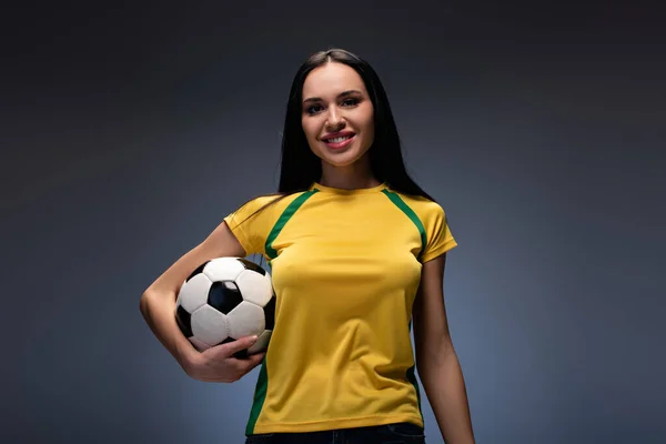 Hermosa joven sonriente sosteniendo pelota de fútbol en gris - foto de stock