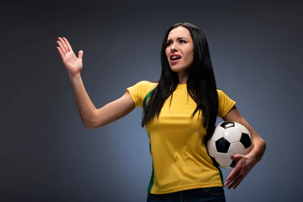 Hermosa chica enojada sosteniendo pelota de fútbol en gris - foto de stock