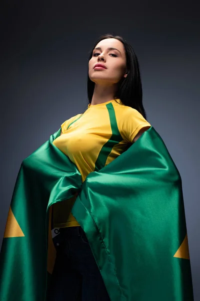 Proud female football fan wrapped in brazilian flag on grey — Stock Photo