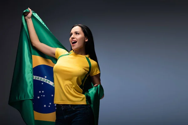 Aufgeregter weiblicher Fußballfan mit brasilianischer Fahne auf grau — Stockfoto