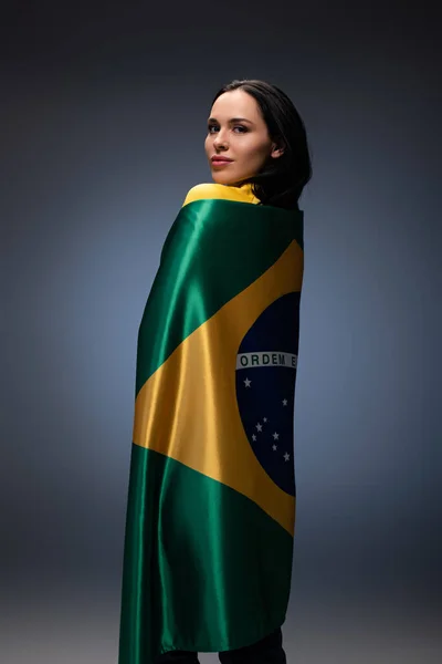Atractivo ventilador de fútbol femenino envuelto en bandera brasileña en gris - foto de stock