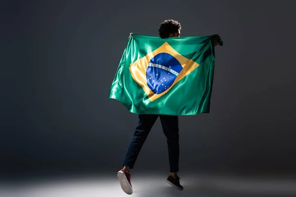 Футбольный болельщик прыгает с бразильским флагом на сером — стоковое фото