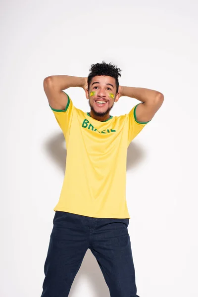 Torcedor de futebol americano africano feliz em camiseta amarela com sinal brasil em pé sobre cinza — Fotografia de Stock
