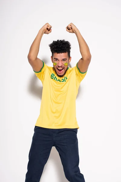 Fan de football afro-américain en t-shirt jaune avec pancarte brésilienne criant et gesticulant sur gris — Photo de stock