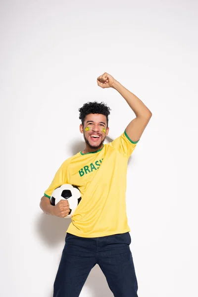 Happy african american football fan in yellow t-shirt holding ball on grey — Stock Photo