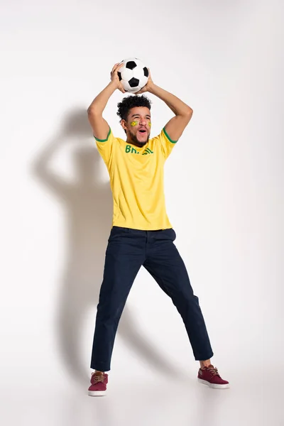 Excited african american football fan in yellow t-shirt holding ball on grey — Stock Photo