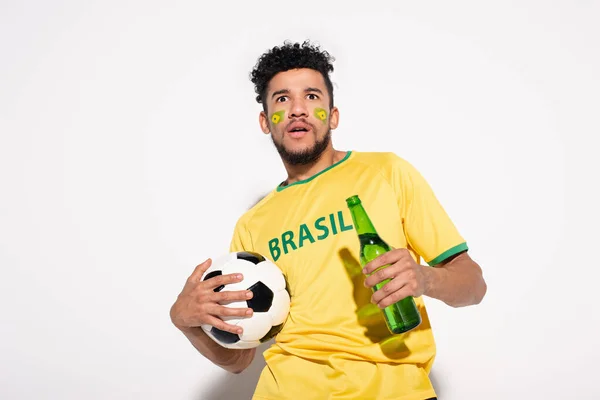 Chocado afro-americano fã de futebol segurando bola e garrafa de cerveja em cinza — Fotografia de Stock