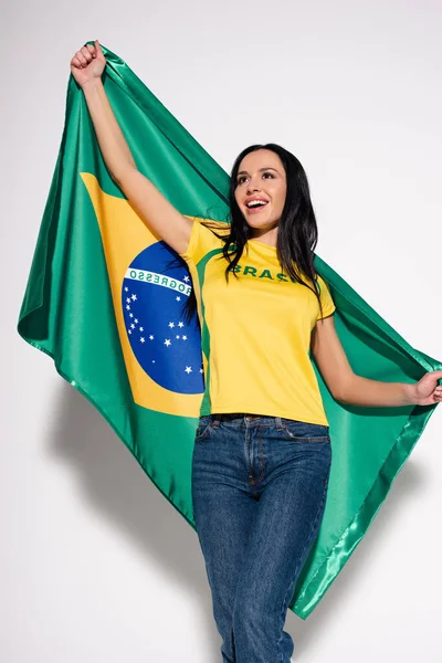 Весела жінка-футболістка тримає бразильський прапор на сірому — стокове фото