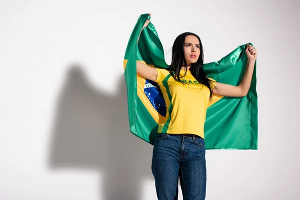 Ventilador de futebol feminino preocupado segurando bandeira brasileira em cinza — Fotografia de Stock