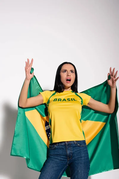 Shocked female football fan holding brazilian flag on grey — Stock Photo