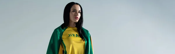 Панорамний знімок привабливого вентилятора жіночого футболу, загорнутого в бразильський прапор ізольовано на сірому — стокове фото