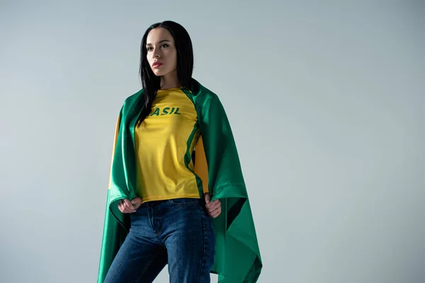 Жіночий футбольний вентилятор, загорнутий в бразильський прапор ізольований на сірому — стокове фото