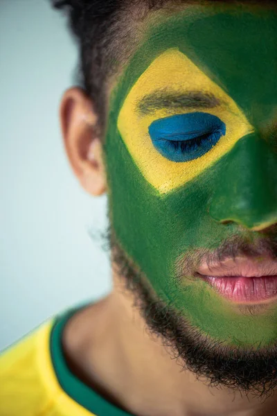 Apuesto fanático del fútbol afroamericano con los ojos cerrados y la cara pintada como bandera brasileña aislada en gris - foto de stock