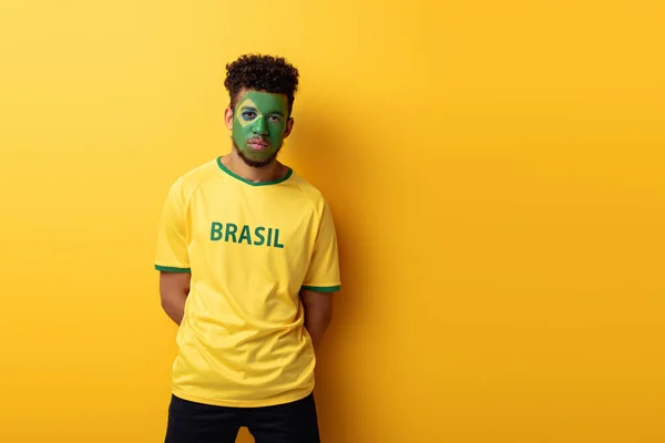 Abanico de fútbol americano africano con la cara pintada en camiseta con signo de Brasil en amarillo - foto de stock