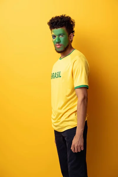 Fã de futebol americano africano com rosto pintado como bandeira brasileira em amarelo — Fotografia de Stock