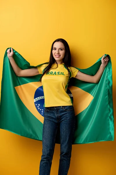 Fan de fútbol femenino feliz sosteniendo bandera brasileña en amarillo - foto de stock