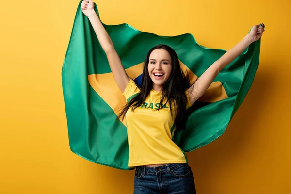 Fã de futebol feminino animado segurando bandeira brasileira no amarelo — Fotografia de Stock