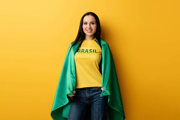 Abanico de fútbol femenino sonriente envuelto en bandera brasileña en amarillo - foto de stock