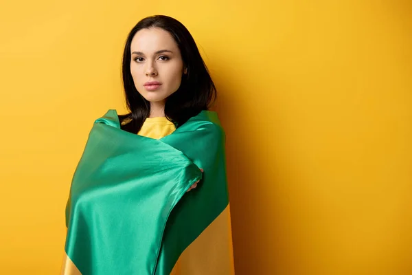 Beautiful female football fan wrapped in brazilian flag on yellow — Stock Photo