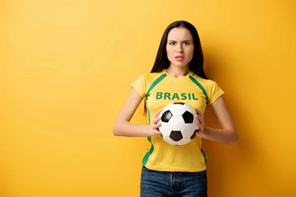Stressed female football fan holding ball on yellow — Stock Photo