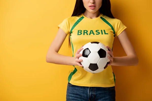 Обрізаний вид злий жіночий вентилятор футболу тримає м'яч на жовтому — стокове фото
