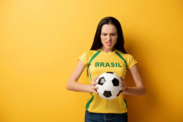 Агрессивная футбольная фанатка держит мяч на желтом — стоковое фото