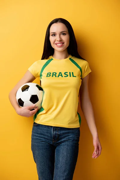 Smiling female football fan holding ball on yellow — Stock Photo