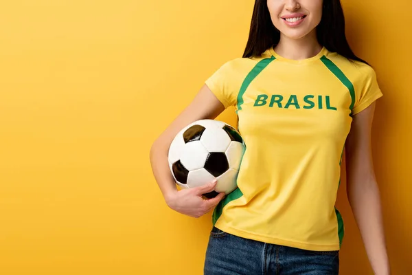 Vista ritagliata del tifoso di calcio femminile sorridente che tiene la palla sul giallo — Foto stock