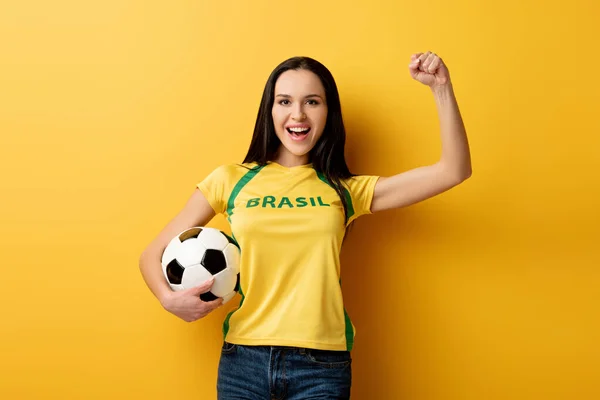 Excitado fã de futebol feminino segurando bola no amarelo — Fotografia de Stock