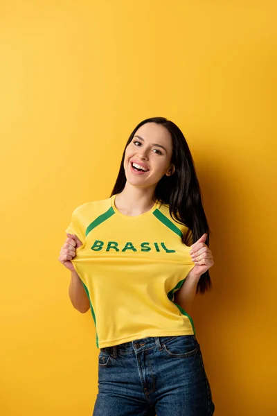 Allegro tifoso di calcio femminile in t-shirt gialla con segno brasiliano su giallo — Foto stock