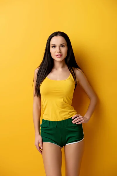 Приваблива молода жінка стоїть в зелених шортах на жовтому — стокове фото